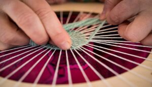 Hands weaving thread on a frame.
